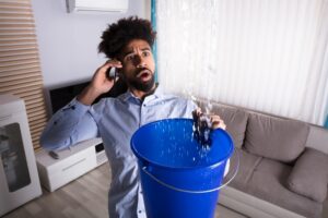 man-calling-a-plumber-while-trying-to-catch-gushing-water-from-a-leak-in-a-bucket